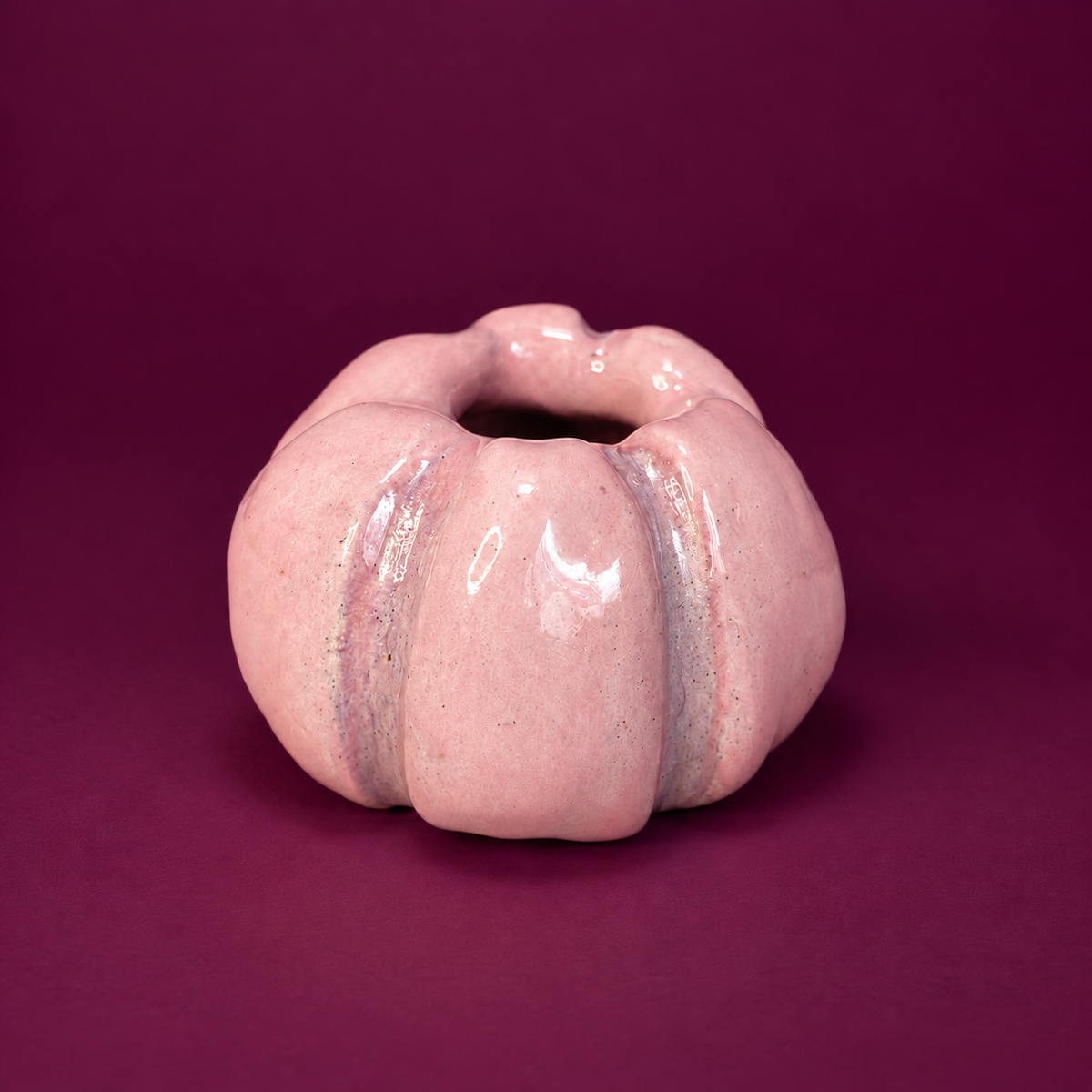 Light pink ceramic pumpkin taper holder with mauve groove details against a plum background.